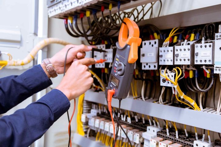 Electrician testing a control panel with a clamp meter